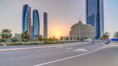 Gökdelenler Abu Dabi batımında Etihad Kuleleri binalar timelapse ile aydınlatılmış. Avuç içi ve yolda trafik Park. Abu Dhabi Birleşik Arap Emirlikleri ikinci en kalabalık kenti başkentidir