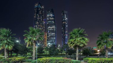 Abu Dabi Etihad Kuleleri binalar timelapse ile gece ışıklı gökdelenler. Avuç içi park. Abu Dhabi Birleşik Arap Emirlikleri ikinci en kalabalık kenti başkentidir