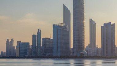 Abu Dabi şehri gün doğumundan sonra gökdelenlerle gökdelenler arasında yükseliyor. Kültür köyü yakınlarındaki dalgakırandan gelen su yansıması zamanlamasıyla birlikte. Güneş modern binalara yansıdı. Sabah gökyüzünde çok az bulut