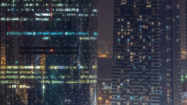 Cam ve çelik ofis ışıklandırmalarından oluşan çok katlı gökdelenlerin ve zaman ayarlı insanların pencereleri. Dairelerde yanıp sönen ışıklar. Abu Dabi, BAE