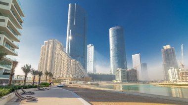 Abu Dabi 'deki Al Reem Adası' ndaki gökdelenler plajdan hiperhızlandırılmış zaman dilimi. Al Reem Adası sakinleri sabah sisli ve ışık ışınlarıyla cam bir yüzeye yansıyor.