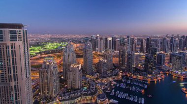 Mavi gökyüzü ile açık bir akşamda Dubai Marina 'da yatlar gece gündüz saatlerinde parlayan ışıklar ve en yüksek gökdelenler.