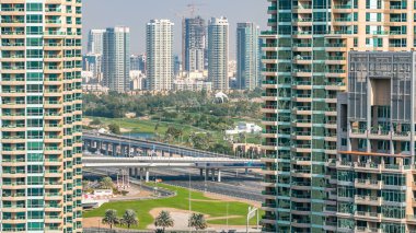 Golf sahasında gündüz vakti Şeyh Zized yolunda trafik varken. Golf sahasının yeşil çimenleri arka planda şehrin gökdelenleri gün batımında. Yan taraftaki modern kuleler