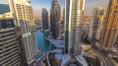 Yol timelapse üzerinde üstten görünüm binaların Jumeirah Lakes Towers trafik ile gün batımında. Jlt 79 kuleleri 3 yapay göl ve park kenarları boyunca inşa ediliyor oluşan büyük bir gelişmedir. Gökdelen üzerinden üstten görünüm. 