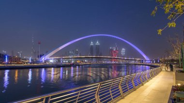 Dubai Creek Deira, Downtown Dubai ve Safa Park ile dokuma Jumeirah Plajı'na bağlayan gece geçiş timelapse Dubai su kanalı gününe ışıklı yaya köprüsü. Gökdelenler manzarası. Dubai, Birleşik Arap Emirlikleri