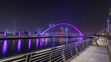Işıklı yaya köprüsü üzerinde Dubai su kanalı gece timelapse hyperlapse alan gezinti yolu üzerinde gökdelenler manzarası. Jumeirah Beach Deira, Downtown Dubai ve Safa Park ile dokuma Dubai Creek bağlandığı. Dubai, Birleşik Arap Emirlikleri