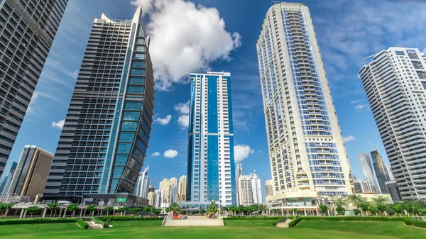 Residential buildings in Jumeirah Lake Towers timelapse in Dubai, UAE.  The JLT is a large development which consists of 79 towers with 3 artificial lakes and park. View with blue cloudy sky from park