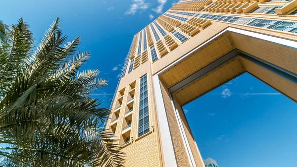 Yellow Luxurious Residence and Business Buildings with arch timelapse in Dubai Marina, UAE. Palm and blue cloudy sky