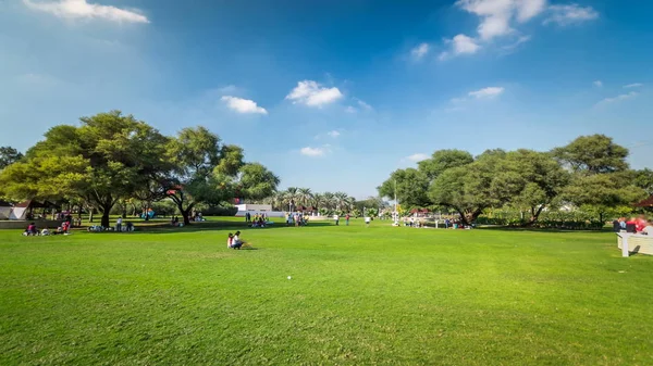 Alley with green lawn and trees at Dubai Creek park timelapse. Dubai, United Arab Emirates. Blue cloudy sky