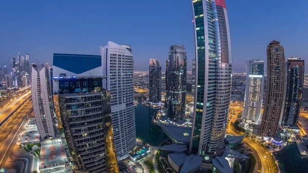 Buildings of Jumeirah Lakes Towers after sunset with traffic on the road day to night transition timelapse. The JLT is a large development which consists of 79 towers being constructed along the edges of 3 artificial lakes and park. Top view from sky