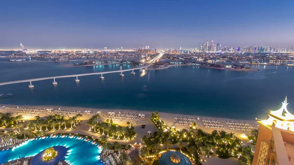 Jumeirah Palm island day to night transition timelapse after sunset in Dubai, UAE. Jumeirah Palm is artificial and unique island in Dubai with skyscrappers on the background. Villas and monorail train top view from atlantis