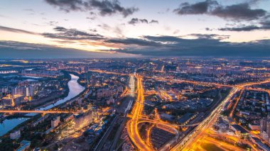 Aerial top view of Moscow city day to night transition timelapse after sunset. Form from the observation platform of the business center of Moscow City. Moscow river and traffic on roads at summer day clipart