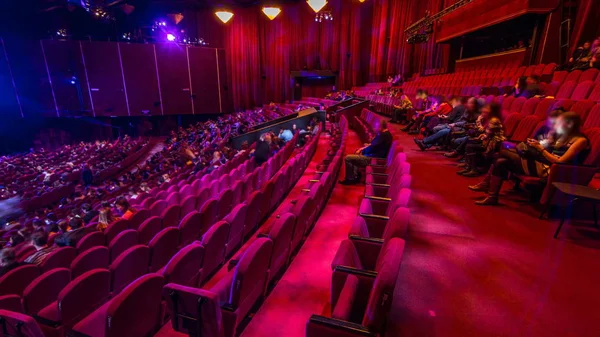 观众聚集在礼堂 Timelapse 剧院的演出 大大厅与红色扶手椅位子 观众在关闭灯之前填充位置 从右侧查看 — 图库照片
