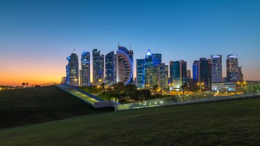 Doha 'nın yüksek katlı mahallesi, gün batımından sonra, yeşil çimenlik ve ön planda yapay tepe ile Hotel Park' tan görülebilen, gece-gündüz zaman geçişi. Gökdelenler ve palmiyeler