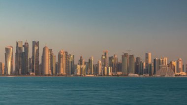 Katar 'ın Doha şehrinin ufuk çizgisi sabahın erken saatlerinde güneşin zengin ılık renkleri cam gökdelenlerden yansıyor..