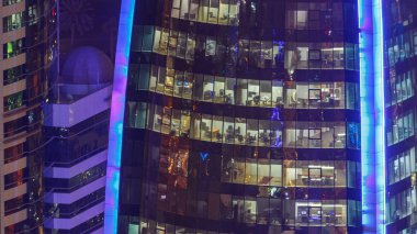 İçerideki cam ve çelik ofis aydınlatması ve çalışan insanların çok katlı binasının zaman çizelgesi. Gökdelenlerin gece aydınlanması. Doha, Katar