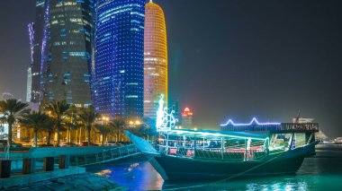 Geleneksel dhow botu Doha 'da, arka planında modern binalar olan gece zaman diliminde. Batı körfezinde aydınlık gökdelenler.