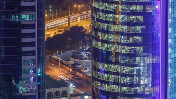 İçerideki cam ve çelik ofis aydınlatması ve çalışan insanların çok katlı binasının zaman çizelgesi. Gökdelenlerin gece aydınlanması. Yollarda trafik vardı. Doha, Katar
