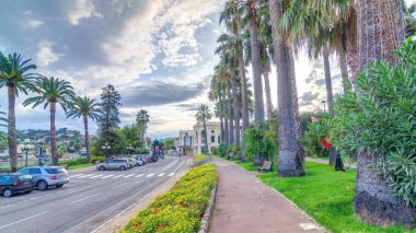 Avuç içi akşam görünümüne Beaulieu-sur-Mer timelapse hyperlapse center Caddesi üzerinde. Günbatımı gökyüzü bulutlu arka plan üzerinde. Casino ve Binalar yakın. Yolda trafik