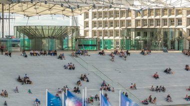 Merdivenleri olan Büyük Kemer ve üzerinde oturan insanlar Fransa, Paris 'in Savunma İş Bölgesi' nde zamanlarını ayarlıyorlar. Yaz günü mavi bulutlu bir gökyüzü. Üst görünüm