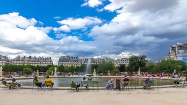 İnsanlar Tuileries Sarayı 'nda Louvre Müzesi yakınlarındaki açık hava parkında dinleniyorlar. Dönme dolaba bak. Bulutlu mavi gökyüzü ile yaz günü sahnesi. Paris, Fransa