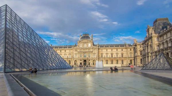 噴水のある大きなガラスのピラミッドとルーブル美術館の中庭は 日没前に過経過します 青空を背景に夏の日を歩く観光客 フランス — ストック写真