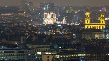 Paris 'te bir gece vakti çatıların üstündeki hava manzarası. Aydınlatılmış Notre Dame de Paris ve Saint-Sulpice manzaralı. Işıklar sönüyor.