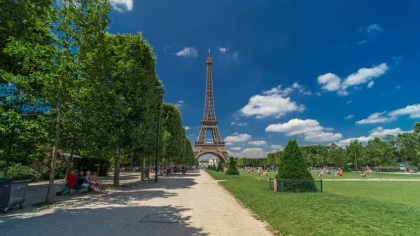 Paris 'teki Champs de Mars' taki Eyfel Kulesi. Zaman atlaması, Fransa. Yazın mavi bulutlu gökyüzü Yeşil çimenler ve etrafta yürüyen insanlar