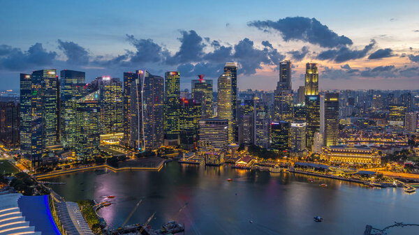 A view of Singapore business district skyscrapers at evening with water reflections day to night timelapse. Aerial top view of illuminated towers with blinking lights in windows