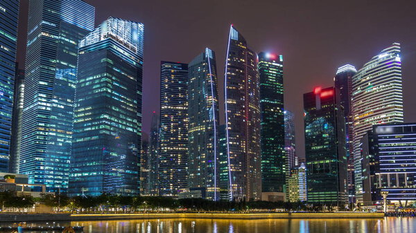 A view of Singapore business district skyscrapers in the night time with water reflections timelapse hyperlapse. Illuminated towers with blinking lights in windows