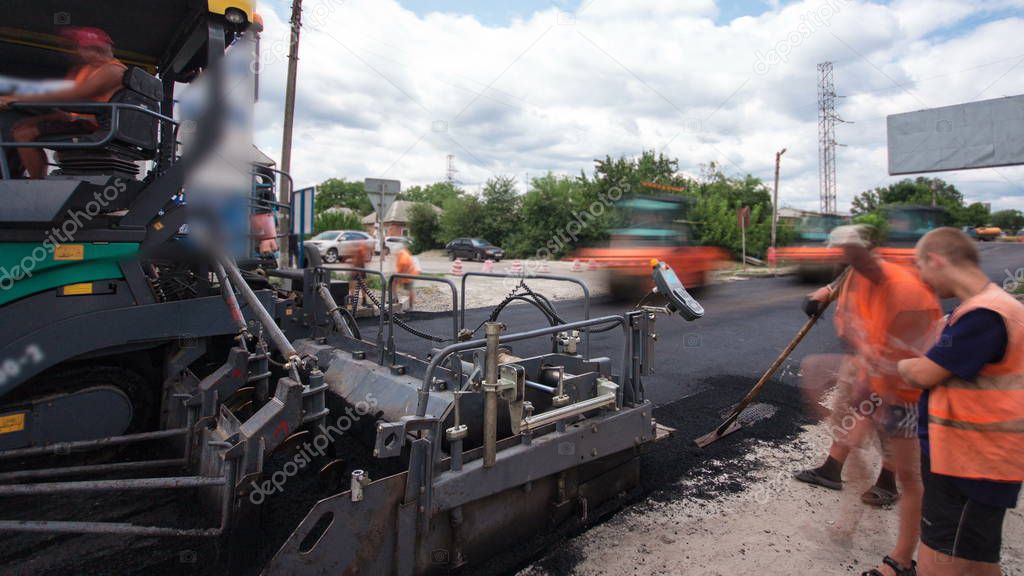 A paver finisher, asphalt finisher or paving machine placing a layer of asphalt during a repaving construction project timelapse. Trucks with asphalt
