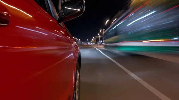Drivelapse from side of fast car moving on a night avenue in city timelapse hyperlapse, road with lights reflected on car on high speed. Rapid rhythm of a modern city.