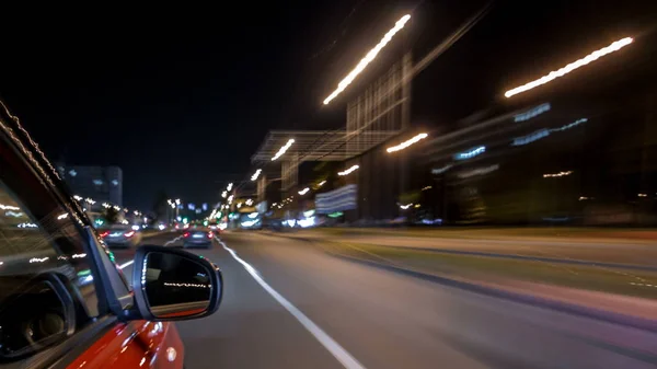 Drivelapse from side of fast car moving on a night avenue in city timelapse hyperlapse, road with lights reflected on car on high speed. Rapid rhythm of a modern city.