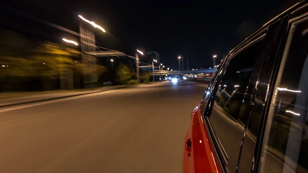 Drivelapse from side of fast car moving on a night avenue in a city timelapse hyperlapse, road with lights reflected on car at high speed. Rapid rhythm of a modern city.