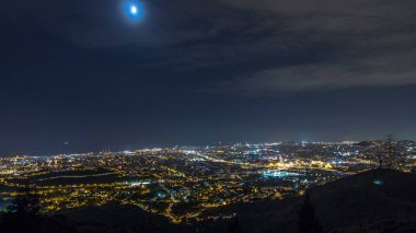 Barcelona and Badalona skyline with roofs of houses and sea on the horizon night timelapse. Aerial view from Iberic Puig Castellar Village viewpoint on top of hill clipart