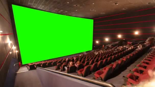 Kinosaal mit Zuschauern, roten Stühlen und grüner Projektionswand im Zeitraffer. Menschen füllen leere Halle und setzen sich sehr schnell an ihren Platz