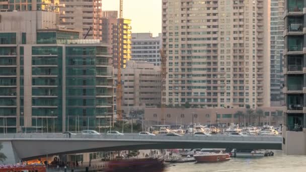 Yachts and boats with tourists staying near shoping mall and passing under a bridge in Dubai Marina district timelapse. — Stock Video