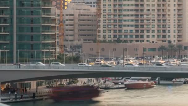 Yachten und Boote mit Touristen, die sich in der Nähe von Einkaufszentren aufhalten und im Zeitraffer unter einer Brücke im Yachthafenbezirk Dubai vorbeifahren. — Stockvideo