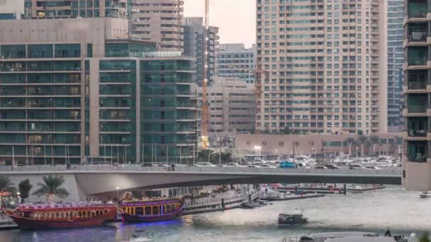 Yachts and boats with tourists staying near shoping mall and passing under a bridge in Dubai Marina district day to night timelapse. — Stock Video