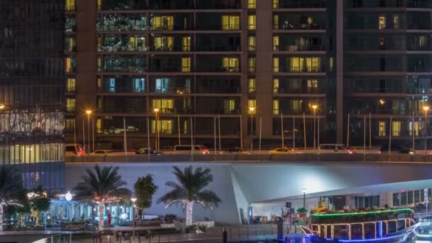 Jachten en boten met toeristen verblijft in de buurt van shoping mall en passeren onder een brug in Dubai Marina district nacht timelapse. — Stockvideo