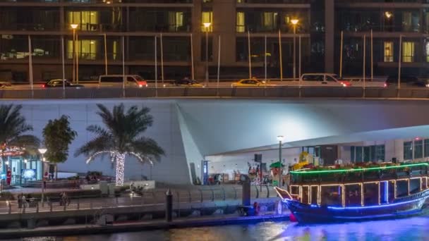 Yachter och båtar med turister vistas nära shoping mall och passerar under en bro i Dubai Marina-distriktet natt timelapse. — Stockvideo