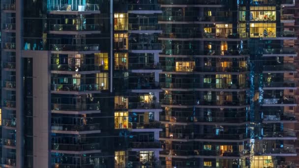 Glowing windows in multistory modern glass residential building light up at night timelapse. — Stock Video