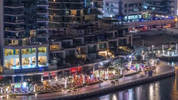 高級ドバイ マリーナ運河を通過する船やレストラン夜のタイムラプス遊歩道 ライトアップされた高層ビルのトップを上から表示します ドバイ アラブ首長国連邦 — ストック動画