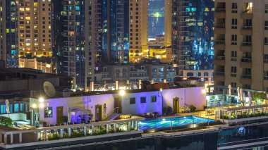 Dubai Marina havadan görünümden bir noktadan gece timelapse. Modern gökdelenler ve konut kuleleri parlayan windows ile aydınlatılmış. Çatı katındaki yüzme havuzu