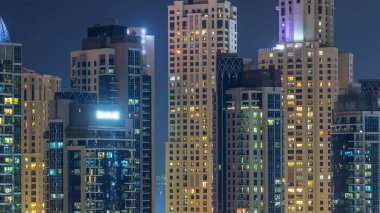 Çok öykülü modern cam ve metal binalar gece timelapse yanar içinde parlayan pencere eşiği. Geceleri aydınlatılan evler. Dubai Yat Limanı ve Jbr, Birleşik Arap Emirlikleri