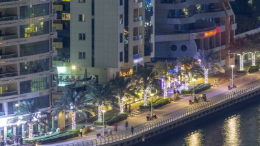 Dubai Marina havadan görünümden bir noktadan gece timelapse. Waterfront adlı mesire üzerinde yürüyen insanlar. Modern gökdelenler ve konut kuleleri parlayan pencerelerle aydınlatılmış