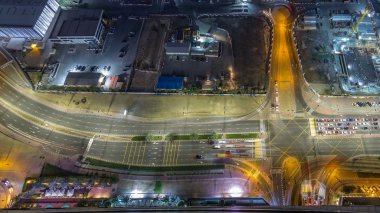 Bir büyük şehir gece timelapse bir yol kavşak hava üstten görünüm. Arabalar ve tramvay hattı ile UAE Dubai Yat Limanı bölgesinin kentsel peyzaj.