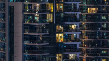 Çok öykülü modern cam konut içinde parlayan pencere eşiği ışık gece timelapse bina. Daireler insanlar. Evler de akşam aydınlatılmış. Dubai Marina, Birleşik Arap Emirlikleri.