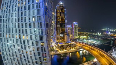 JBR ve Dubai marina hava gece timelapse. Işıklı modern kule ve gökdelen, köprü, yat ve tekne kanalda yüzen trafik