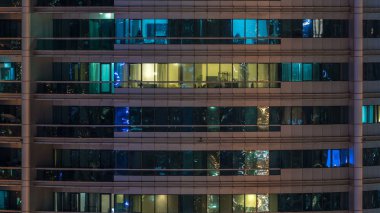 Çok öykülü modern cam konut içinde parlayan pencere eşiği ışık gece timelapse bina. Daireler insanlar. Akşam aydınlatılmış gökdelenler. Dubai Marina, Birleşik Arap Emirlikleri.